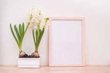 Portrait white picture frame mockup on wooden table. White pot with blooming hyacinths
 hyacinths. White wall background. Scandinavian interior. 
