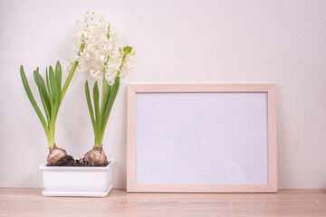 Portrait white picture frame mockup on wooden table. White pot with blooming hyacinths
 hyacinths. White wall background. Scandinavian interior. 
