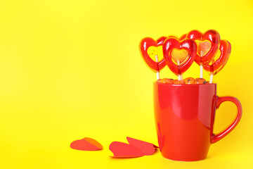 Cup with different candies on yellow background, space for text