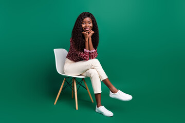 Photo of sweet dreamy curly dark skin woman dressed red shirt sitting chair arms chin isolated green color background