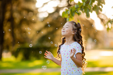 Cute little Asian girl in the summer on a walk blowing soap bubbles