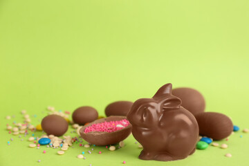 Chocolate Easter bunny, eggs and candies on green background. Space for text