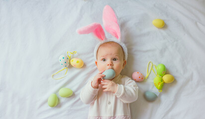 Obraz na płótnie Canvas Cute funny baby with bunny ears and colorful Easter eggs at home on a white background