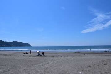 晴れた空と海と浜でくつろぐ人々、右に雲