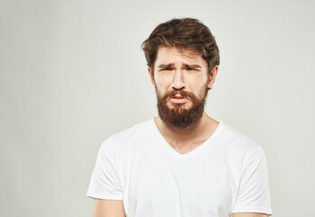 Nice guy with a beard in a white T-shirt on a light background cropped view of a sad face