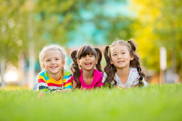 Three little girls of Asian, Indian and European ethnic predation lie on the lawn in the summer. International Children's Day