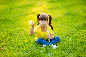Fototapeta premium Cute little Indian girl summer on the lawn blowing soap bubbles
