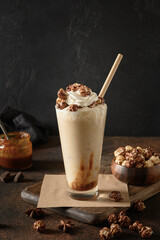 Banana and caramel milkshake garnished whipped cream and popcorn on dark brown background. Vertical...