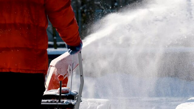 man with a snow blowing machine working in winter day. Man using snowblower to clear snow near residential house after heavy snowfall.