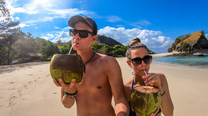 A couple drinking fresh coconut juice, while walking on the idyllic Koka Beach. Hidden gem of Flores, Indonesia. Island life. Happiness and simplicity. Healthy diet. Couple adventurous escapes