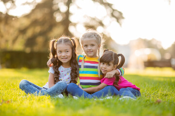 Naklejka na ściany i meble three little girls cuddle in the summer on the lawn. International Children's Day