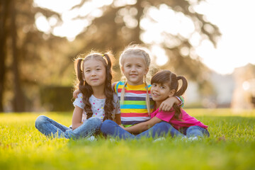 three little girls cuddle in the summer on the lawn. International Children's Day
