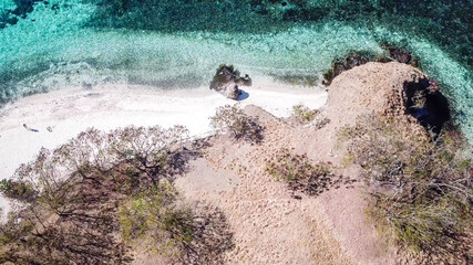 Top down drone shot of a paradise island with some boats anchored around in Komodo National Park, Flores, Indonesia. Brownish island turns into white sand beach and further into green and navy sea