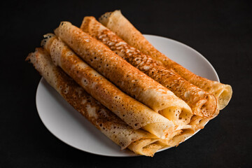 Tasty crepes on a plate on a black background. Traditional Russian food.
