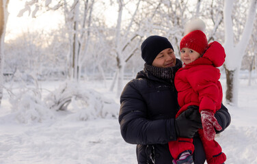 Fototapeta na wymiar A young Caucasian man stands in a winter park and holds his little daughter in his arms. Snowy winter and family.