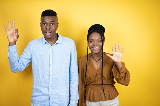 Young african american couple standing over yellow background showing and pointing up with fingers number eight while smiling confident and happy - Powered by Adobe
