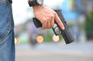 Automatic 9mm pistol holding in hand with blurred street bokeh background. Concept for robbery on the road and security profession.