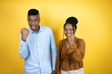 Young african american couple standing over yellow background angry and mad raising fist frustrated and furious while shouting with anger. Rage and aggressive concept.