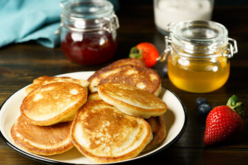 Blini served with strawberry jam, honey, sour cream and fresh berries. Dark wooden table, high resolution