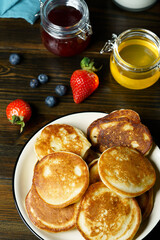 Blini served with strawberry jam, honey, sour cream and fresh berries. Dark wooden table, high resolution