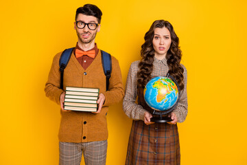 Portrait of attractive bored irritated funky couple holding academic materials globe country world isolated on bright yellow color background
