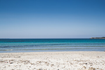 Landscape of an Italian beach in Sardinia. Blue sky, white sand and clear water with no people. Natural view of a sea coastline during summer lockdown due to covid-19 pandemic. Relax and peace concept