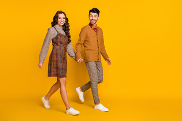 Full size photo of couple go empty space hold hands wear plaid dress pants bowtie sweater isolated on yellow color background