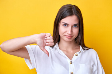 Upset brunette girl showing dislike gesture isolated on yellow background