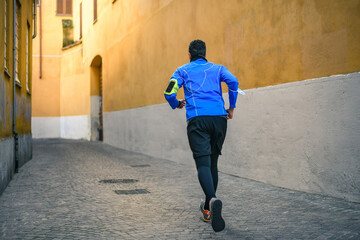 Obraz na płótnie Canvas Male running and listening music during workout. Man run in the city and jogging alone. Runner with mobile phone connected to a smart watch recording data of sport activity with wearable technology.