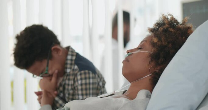 Preteen afro-american boy sitting in hospital ward and crying holding hand of ill mother