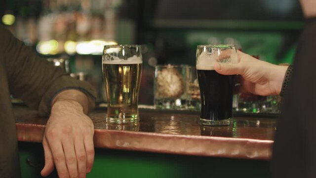 Slow-motion midsection shot of unrecognizable male friends sitting at bar in evening drinking beer