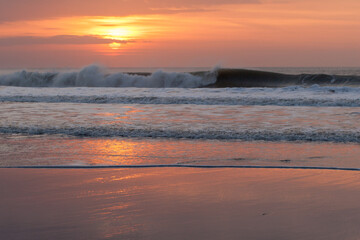 Waves crash against Welcombe Mouth beach in north Devon during sunset. The sunset is reflected in the sand.