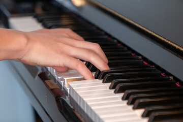 Fototapeta na wymiar Black glossy upright piano with white ivory keys being played with two hands closeup