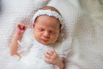 Newborn baby girl sleeping on a white blanket in a dress and wreath.