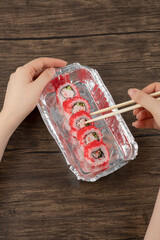 Female hands holding aluminum foil plate of sushi rolls on wooden surface