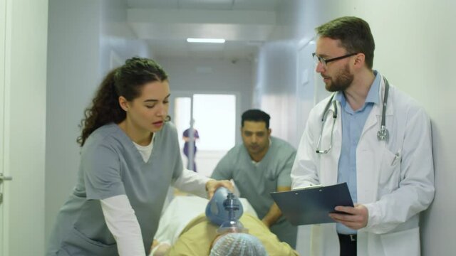 Tilt up shot of paramedics giving ventilation to emergency patient with bag-valve-mask and pushing stretchers towards the camera through hospital