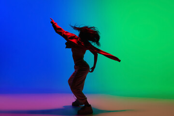 Inspiration. Stylish sportive girl dancing hip-hop in stylish clothes on colorful background at dance hall in neon light. Youth culture, movement, style and fashion, action. Fashionable bright