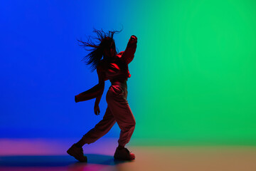 Fototapeta na wymiar Street. Stylish sportive girl dancing hip-hop in stylish clothes on colorful background at dance hall in neon light. Youth culture, movement, style and fashion, action. Fashionable bright portrait.
