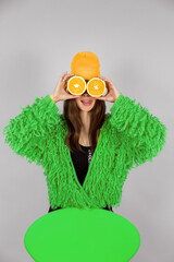 A girl in a bright green fur coat holds oranges.