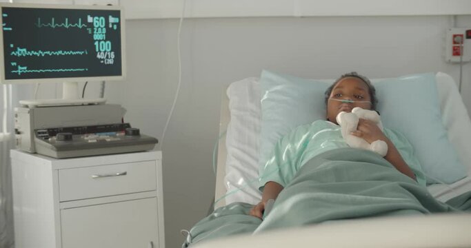 Afro-american kid lying in hospital bed with oxygen tube and plush toy