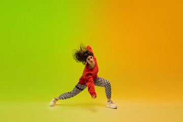 Energy. Stylish sportive girl dancing hip-hop in stylish clothes on colorful background at dance hall in neon light. Youth culture, movement, style and fashion, action. Fashionable bright portrait.