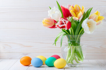 Fototapeta na wymiar Easter eggs and a bouquet of tulips on a wooden table, floral still life. Holiday concept. Greeting card with copy space, empty place for text. Festive template. Bright colorful mockup. Layout.