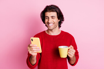 Portrait of attractive cheerful glad guy drinking beverage using device isolated over pink color background