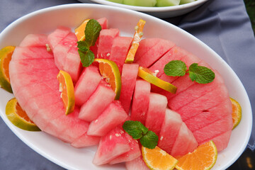 Fresh red watermelon slices on a plate with the addition of fresh orange and mint leaves