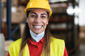 Happy Latin woman working in warehouse while wearing face mask during corona virus pandemic -...