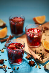 Drinks and cocktails. Mulled wine with cinnamon, star anise, orange, apple and berries in clear glasses on a blue background in bright lighting. Background image, copy space, vertical