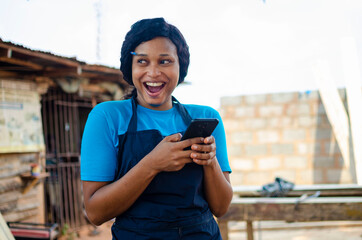 Fototapeta na wymiar young pretty african female carpenter feeling excited as she operates her cellphone