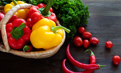 Fresh vegetables - peppers, tomatoes and herbs on a straw plate on a dark background