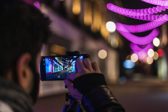 Young man taking a picture in the street at night time.