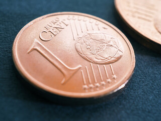 A one euro cent coin lies on a dark blue-gray surface. Money close-up. Illustration on economic or financial theme. The withdrawal of small coins from circulation and the rounding of price tags. Macro
